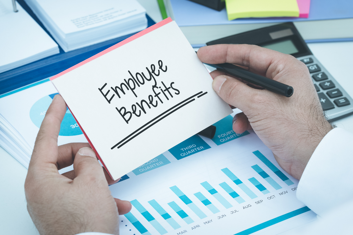 Image of cluttered desk and hands holding a piece of paper that reads "Employee Benefits"