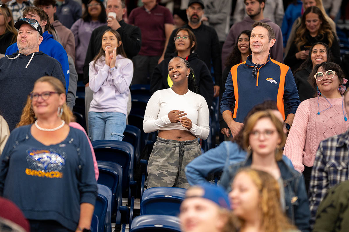 A diverse crowd stands and applauds in a stadium seating area.