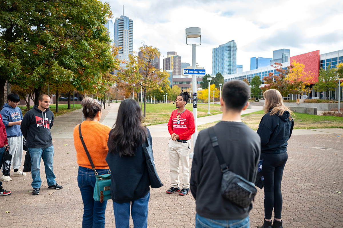 A campus tour guide in a red Office of Admissions sweatshirt leading a group tour outdoors.