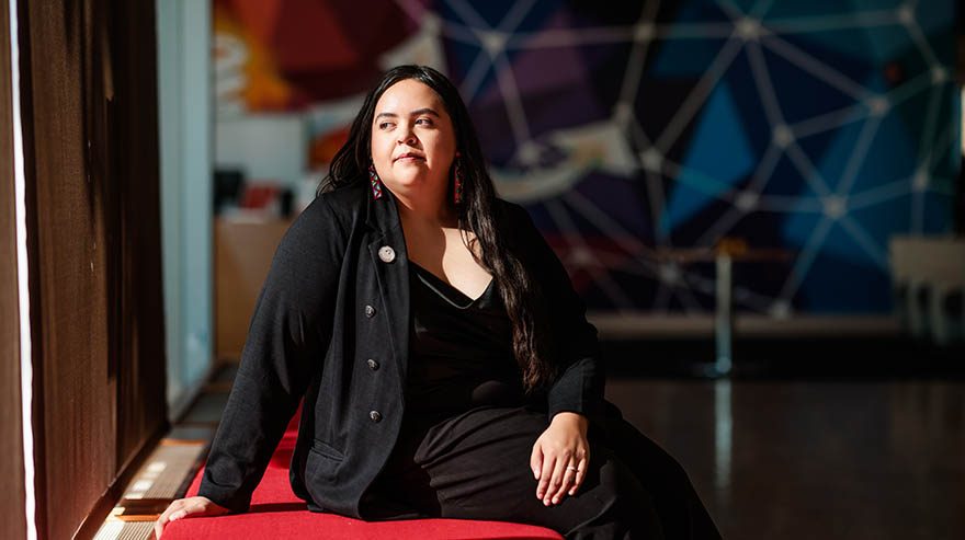 Shayla Bischoff sitting on a red bench indoors, looking off to the side with a colorful mural in the background.