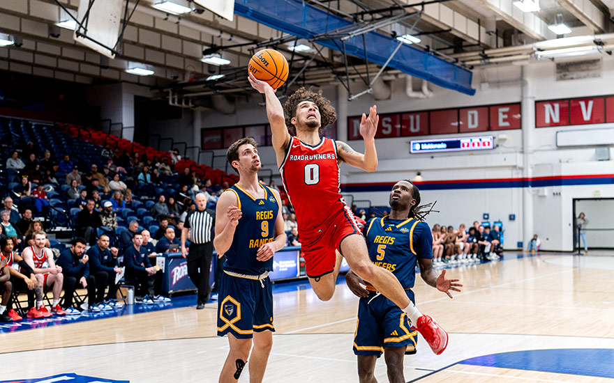 Roadrunner basketball player shoots a layup surrounded by two defenders.