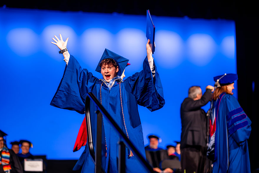 Graduate celebrates during commencement ceremony, holding degree over his head.