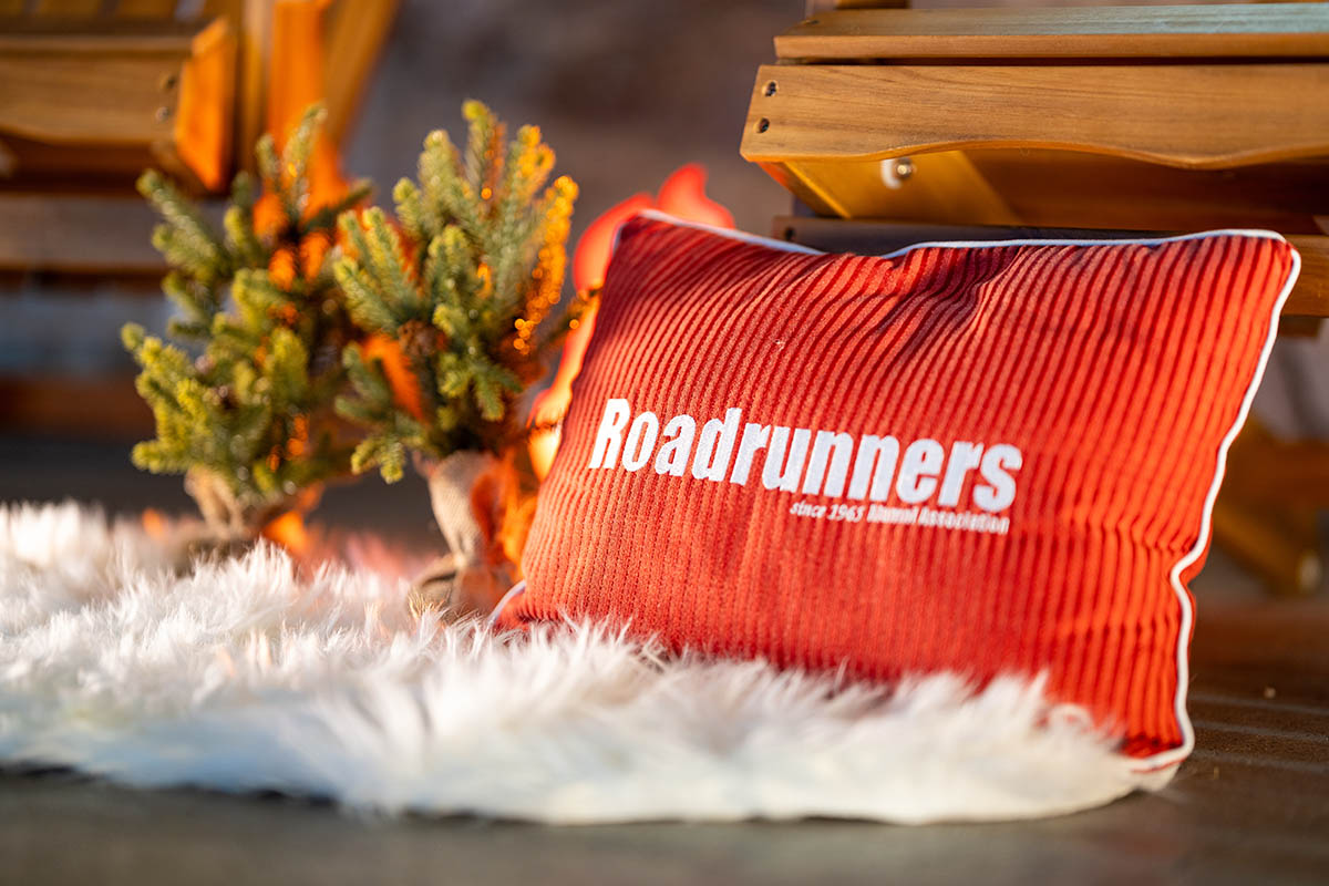 A red "Roadrunners since 1965 Alumni Association" pillow on a fluffy white rug, surrounded by festive holiday decor.