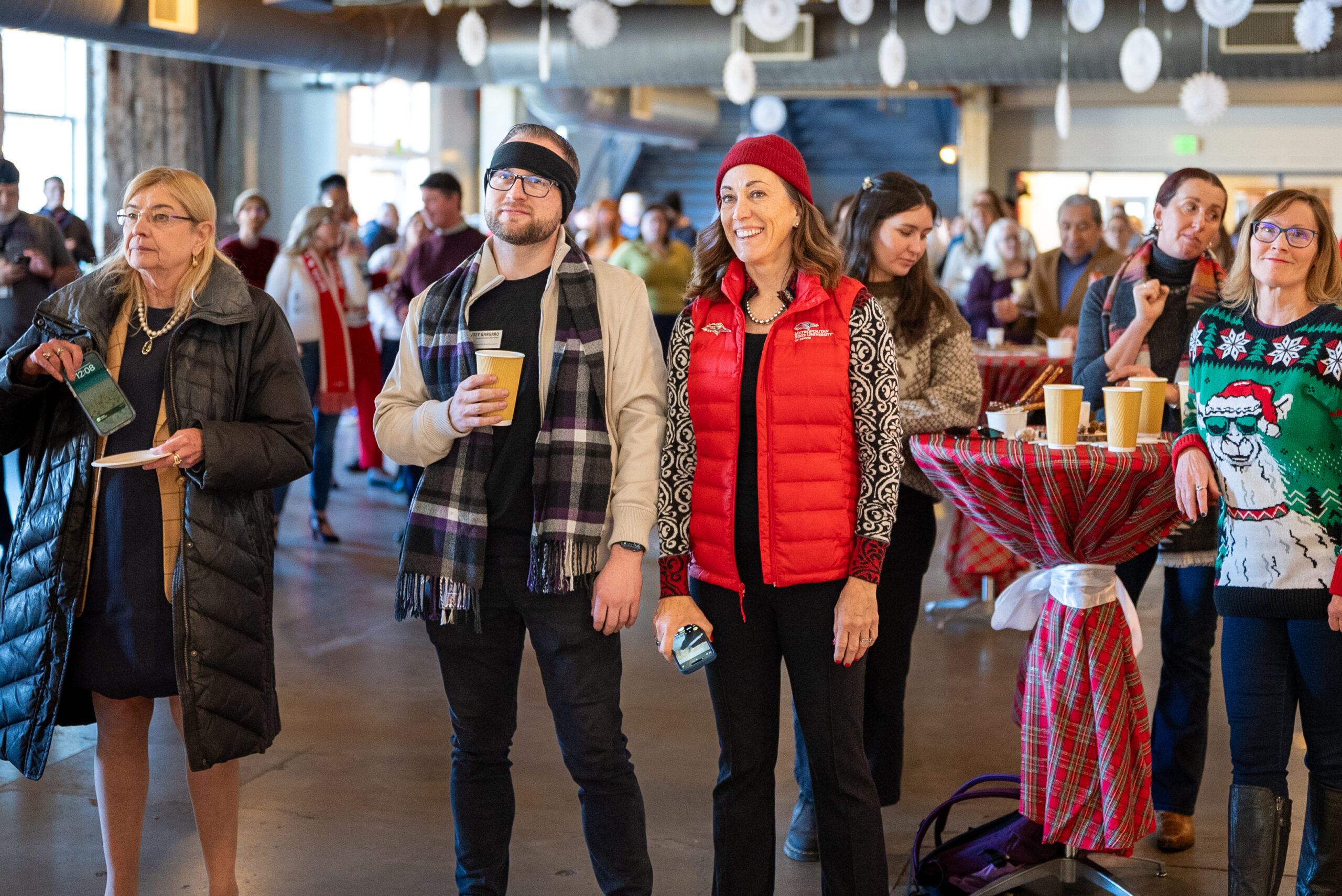 Attendees standing near a table at a holiday event, holding drinks and enjoying the festive atmosphere.