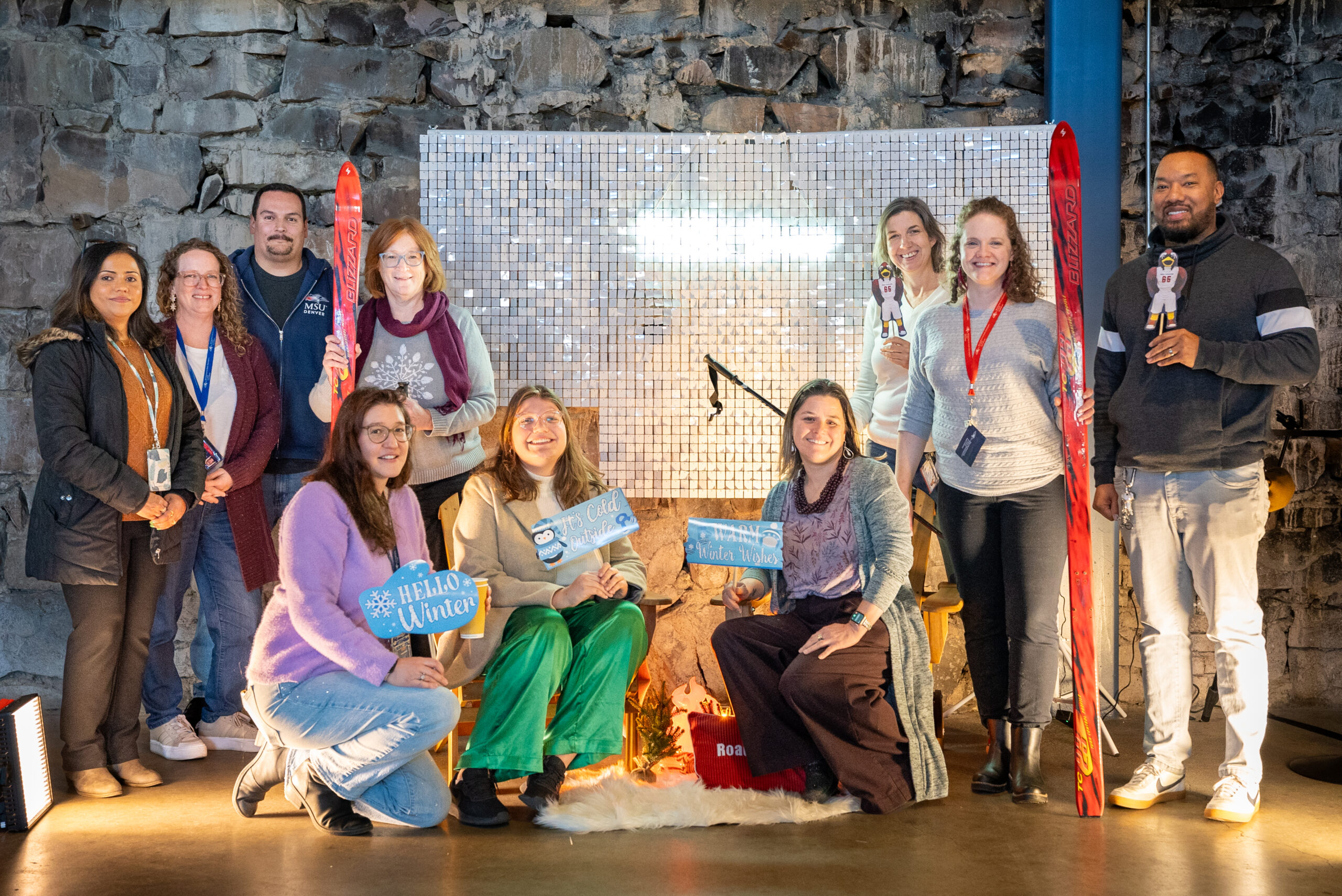 A group poses in front of a holiday backdrop with winter-themed props and decorations.