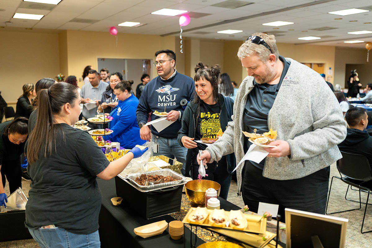 People line up at a buffet table, serving themselves food at a social gathering.