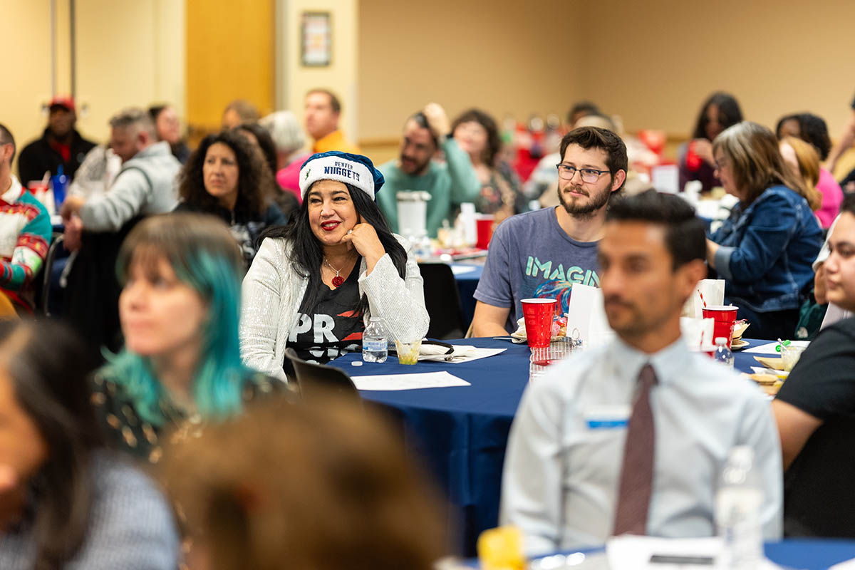 A group of smiling attendees sits together at a round table, surrounded by event decorations and other participants.