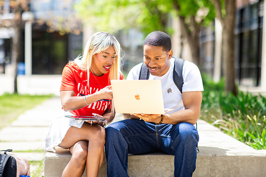 Two students outdoors on the Auraria Campus looking at a computer screen