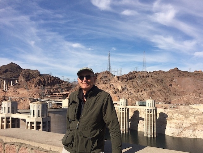 Doug Clark wearing sunglasses and smiling outside in front of a dam