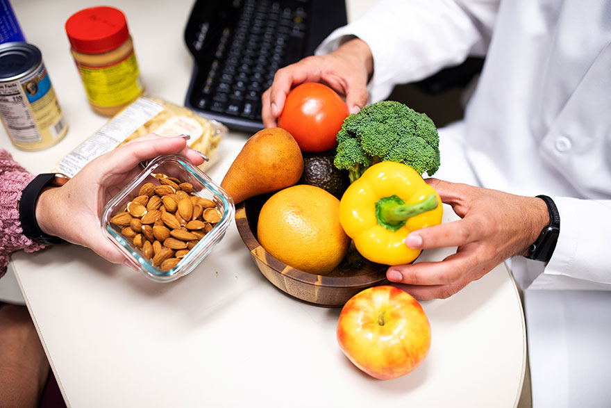 Doctor counsels patient on nutrition, using a bowl of vegetables to demonstrate good eating habits.