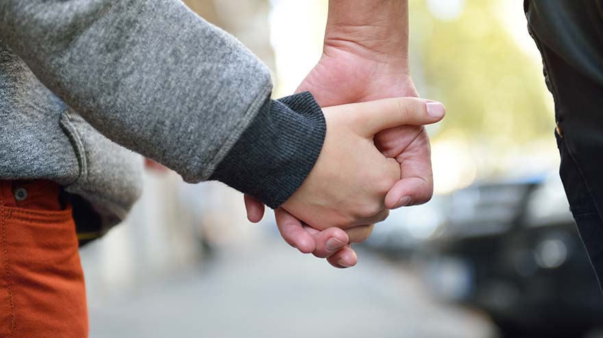 Hands of mother and child outdoor closeup. Mother holds hand of her son walking city.