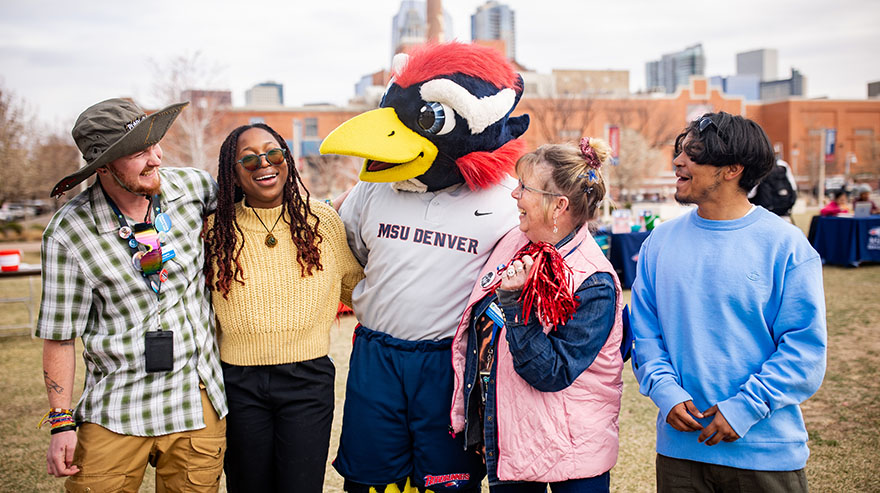 A group of people laughs and poses with Rowdy, the MSU Denver Roadrunner mascot, on the MSU Denver campus.