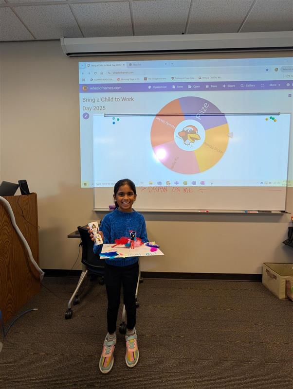 Child presents craft in front a projector screen on Bring a Child to Work Day