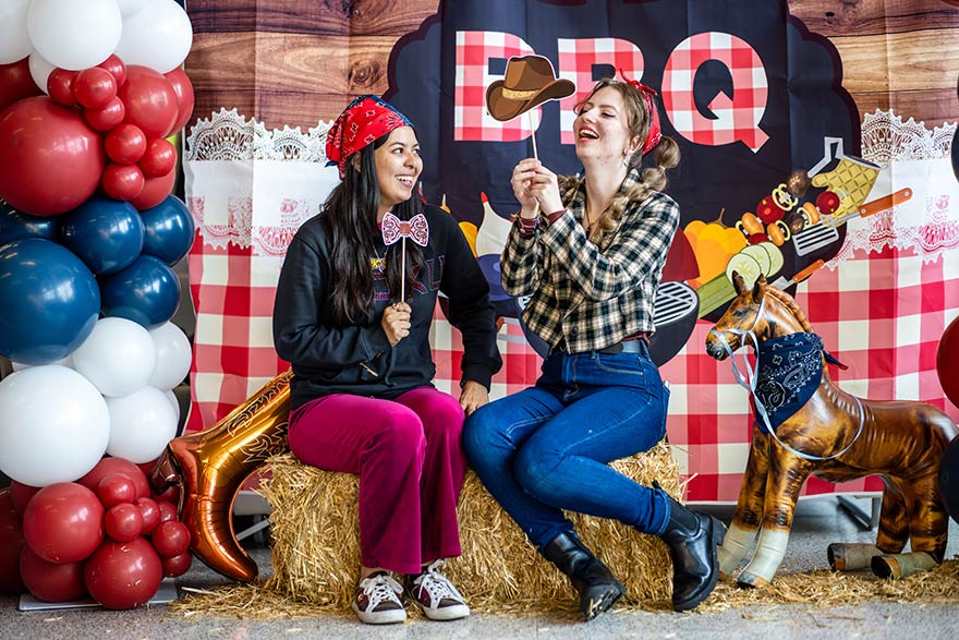 Two MSU Denver employees in western wear pose in front of sign that reads BBQ.