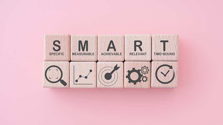 Smart goal for business strategy concept. specific, measurable, achievable, relevant and time-bound text on wooden block with icons on pink background