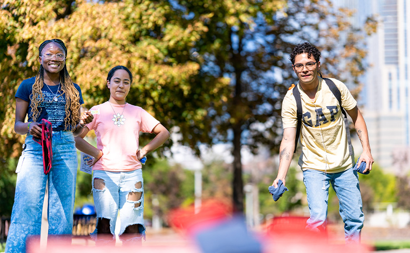 Three students play cornhole on the Auraria Campus on a sunny day