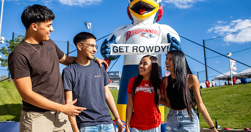 Four students stand smiling in front of a giant inflatable MSU Denver roadrunner holding a “Get Rowdy!” sign.