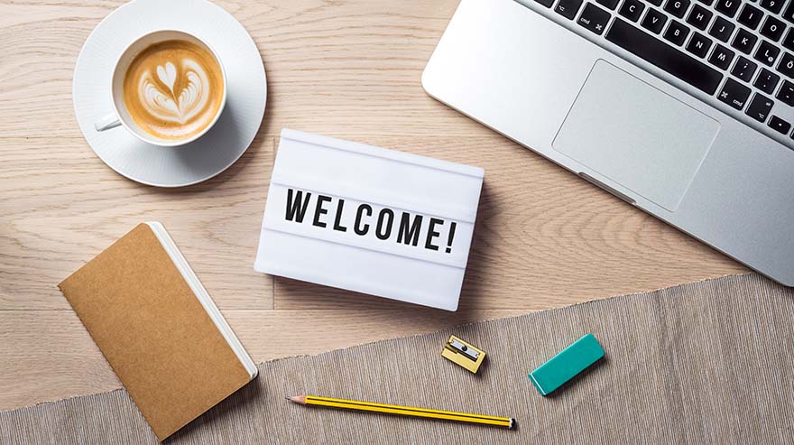 Welcome writing in lightbox lying on wooden desk with office supply and coffee cup as flat lay from bird's eye view