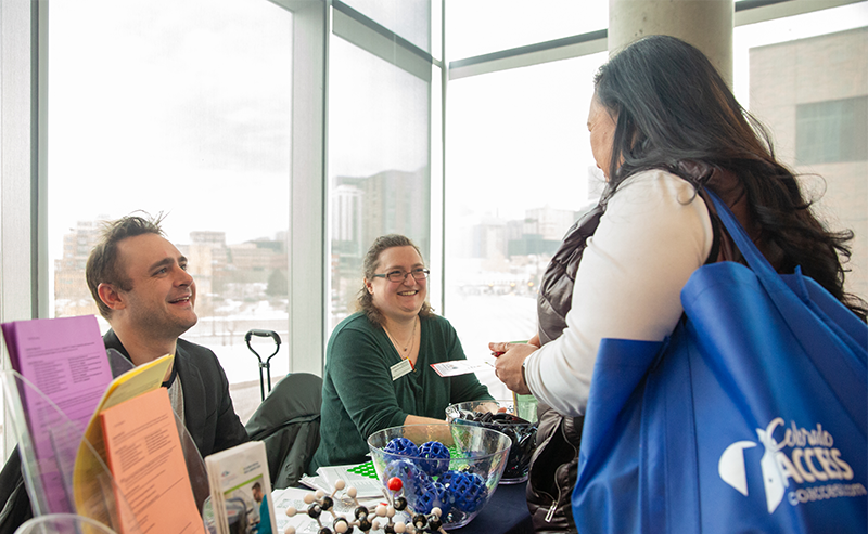 A student engages with two smiling representatives at an MSU Denver event table
