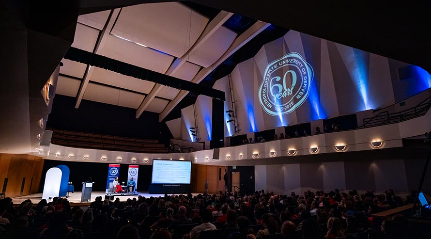 A "60 years of excellence" logo lights up the wall of the King Center concert hall, with President Janine Davidson and Provost Matt Makley on the stage.