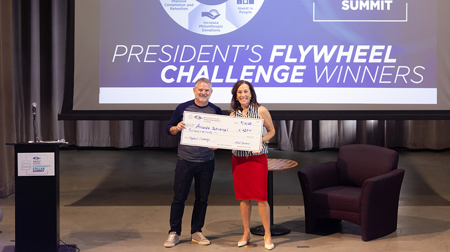 Dr. Janine Davidson and a recipient hold an oversized check on stage during the summit awards ceremony.