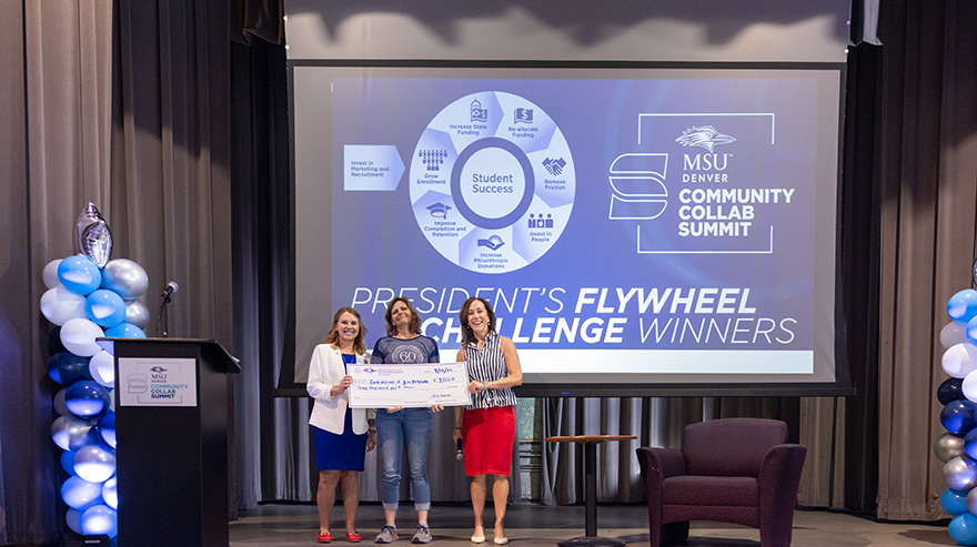 Dr. Janine Davidson stands with two award recipients holding an oversized check at the summit.
