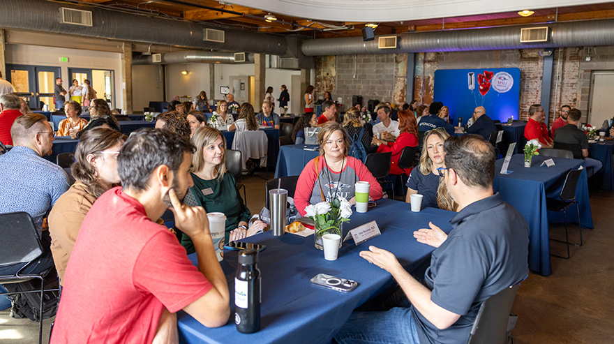 Groups of attendees seated at tables engage in conversation during summit discussions.