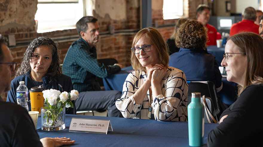 Attendees seated at a table listen during a breakout conversation at the summit.