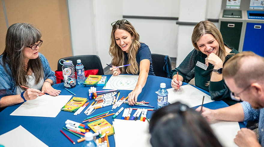 MSU Denver employees collaborate at a table, drawing with markers during a group activity.