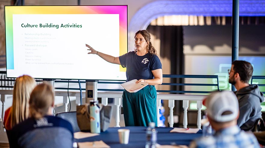 An MSU Denver employee gestures toward a slide titled “Culture Building Activities” while presenting to colleagues.