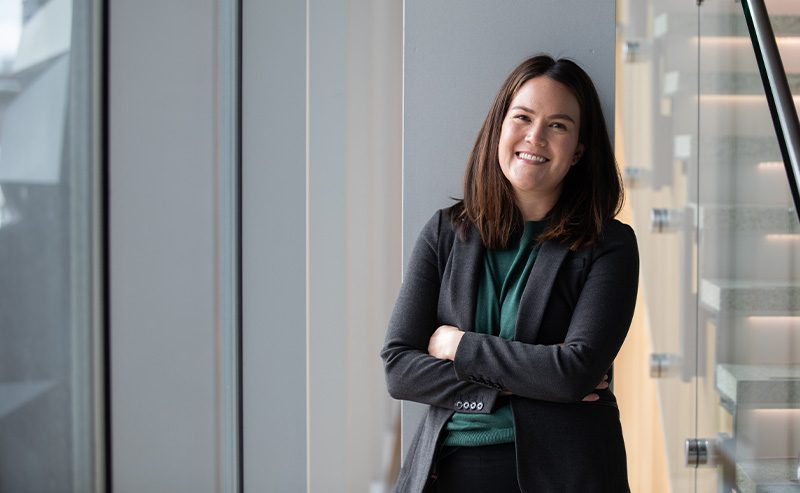 Kaycee Gerhart, Vice President of Government and External Affairs at MSU Denver, smiles while standing with arms crossed near a window.