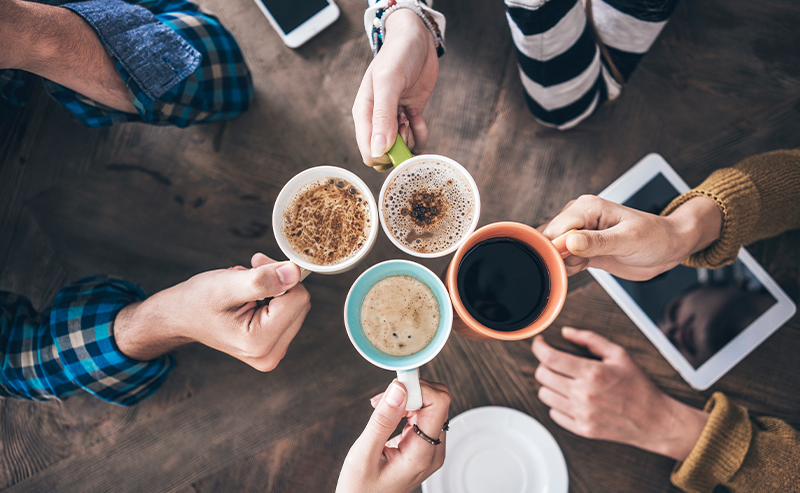 View from above a table with four hands holding cups of coffee.