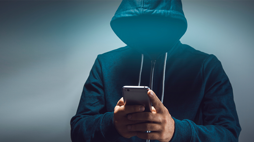 A person wearing a hooded sweatshirt uses a smartphone, representing online security and cybersecurity threats