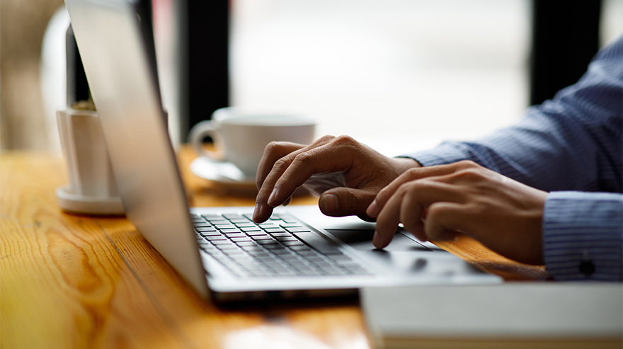 Person types on a laptop at a desk with a coffee cup nearby.