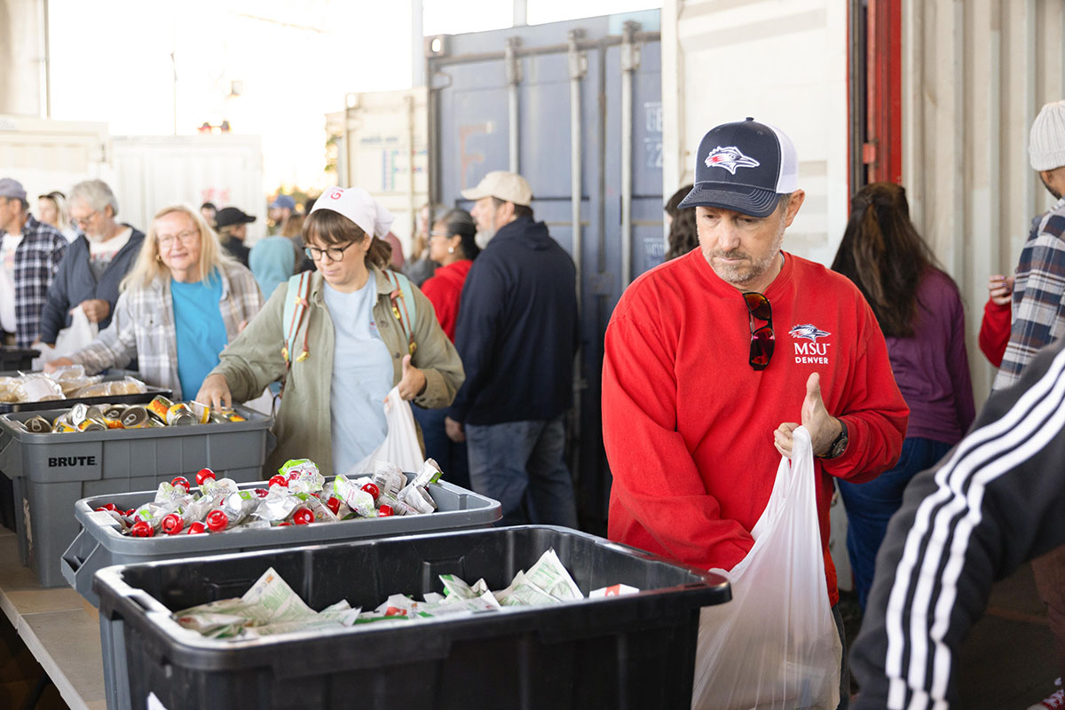 olunteers in a warehouse pack food items into bags among large bins and boxes.