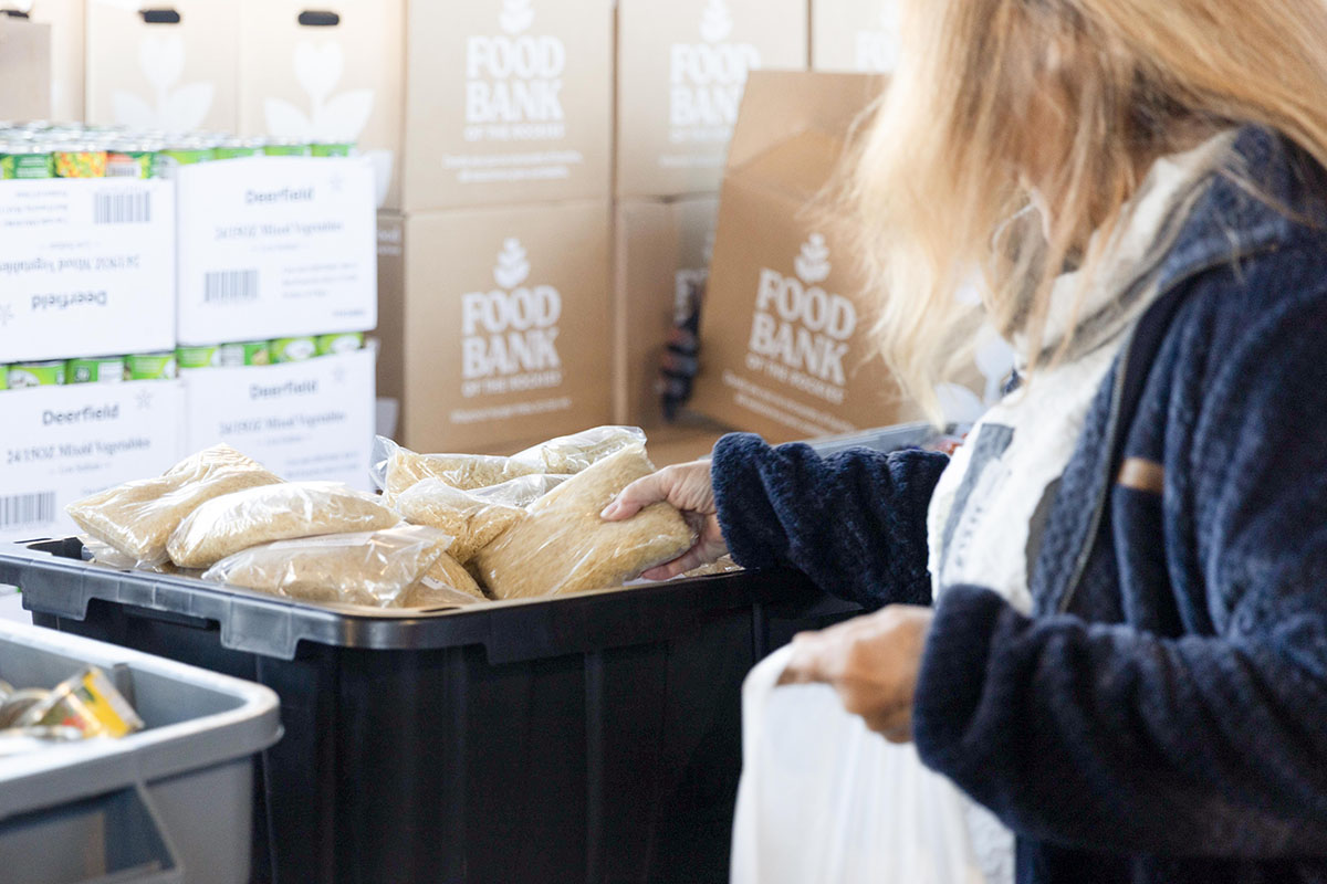 A volunteer places packaged food into a plastic bin labeled “Food Bank.”