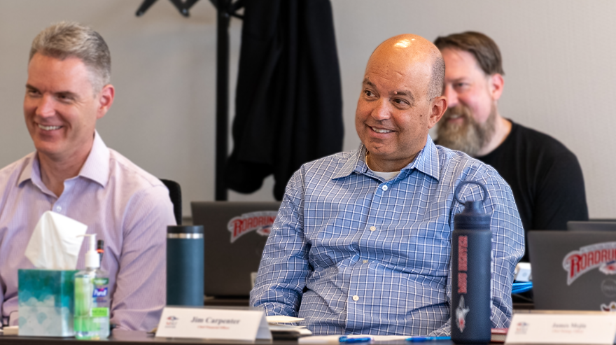 MSU Denver staff members sit and smile during a meeting, with Jim Carpenter at the center of the table