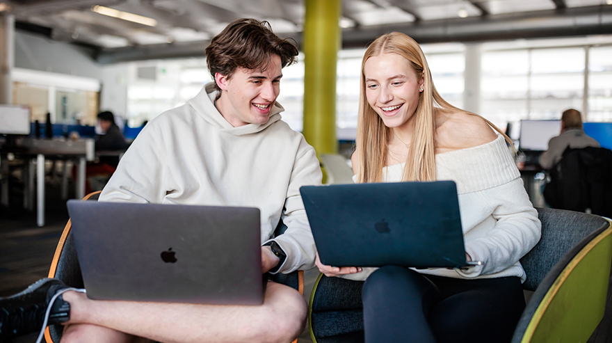 two students talking, with laptop computers open on their laps.