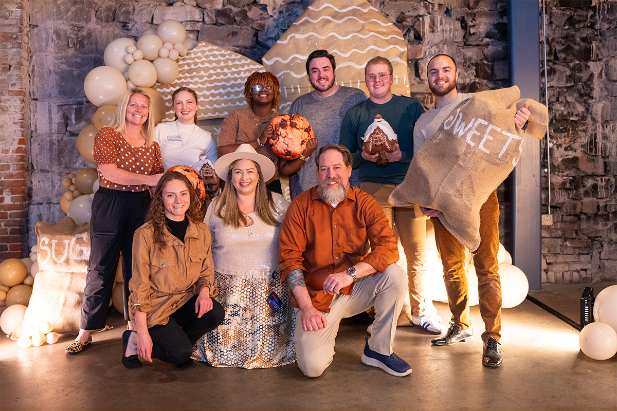 A group of MSU Denver employees pose together in front of a festive holiday backdrop decorated with balloons and gingerbread-themed props.