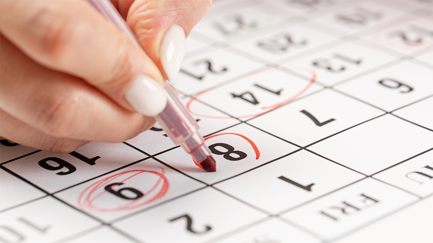 Close-up of a hand marking dates on a calendar with a red pen