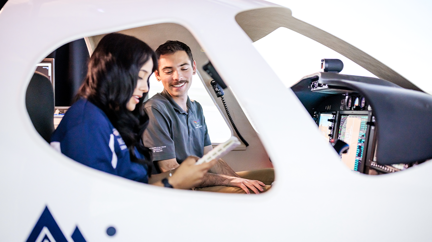 A student and aviation instructor sit inside an aircraft cockpit, reviewing a tablet together during training.