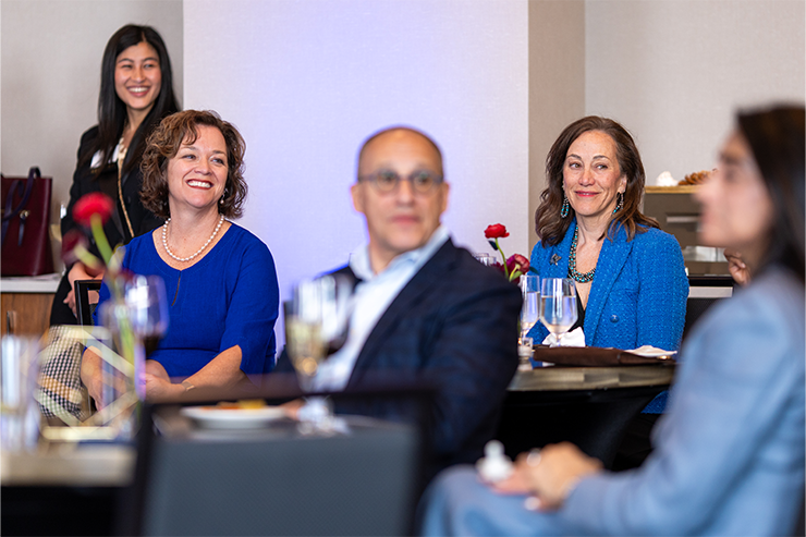 A group of attendees sit at tables during a formal MSU Denver event, listening to a speaker.