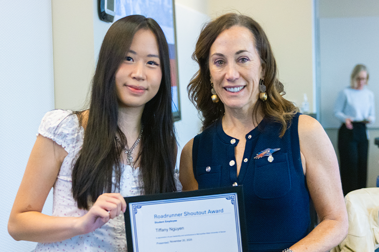 A student stands beside an MSU Denver administrator while holding a framed award during an indoor recognition event.