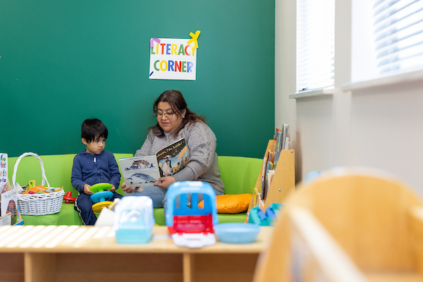 A teacher reads a book to a small child in a literacy learning center.