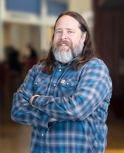 Portrait of Provost Matt Makley smiling with arms crossed, standing indoors with a softly blurred background.