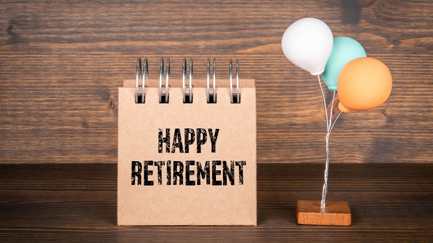 Stock photo of a small desk calendar reading ‘Happy Retirement’ on a wooden surface, next to pastel-colored balloons