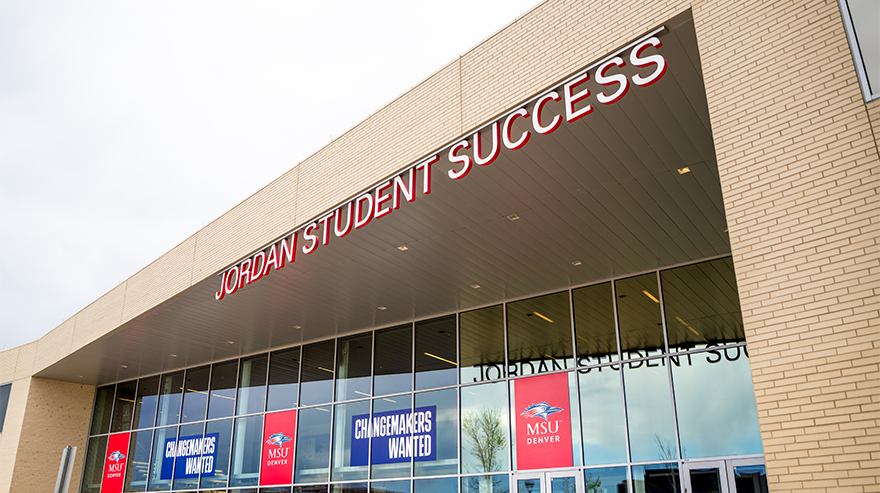The exterior of the Jordan Student Success Building at MSU Denver, with large windows displaying banners that read “Changemakers Wanted.”