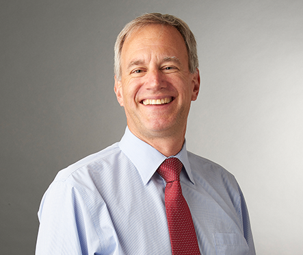 Shaun Schafer smiling in a professional headshot, wearing a light blue dress shirt and red tie against a plain gray background.
