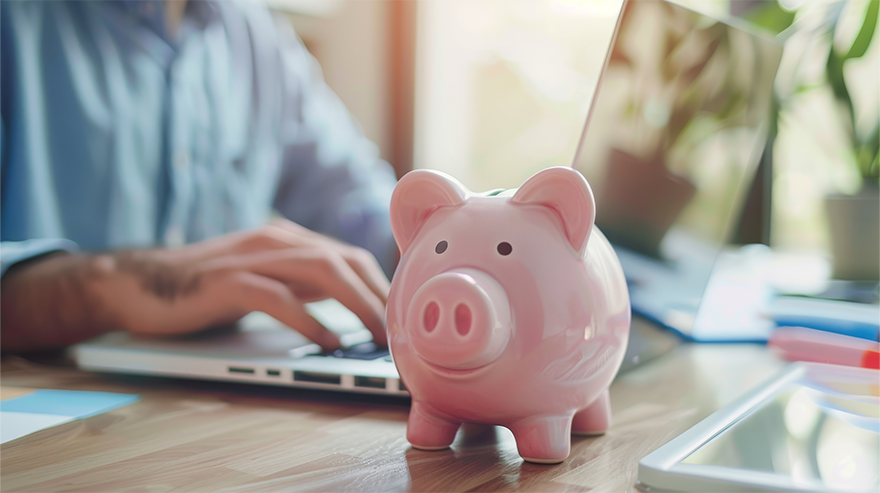 Piggy bank on a desk next to a laptop, representing saving.