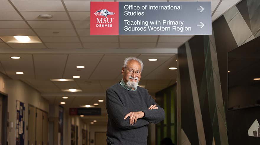 Akbarali Thobhani standing underneath university sign in a class building hallway.